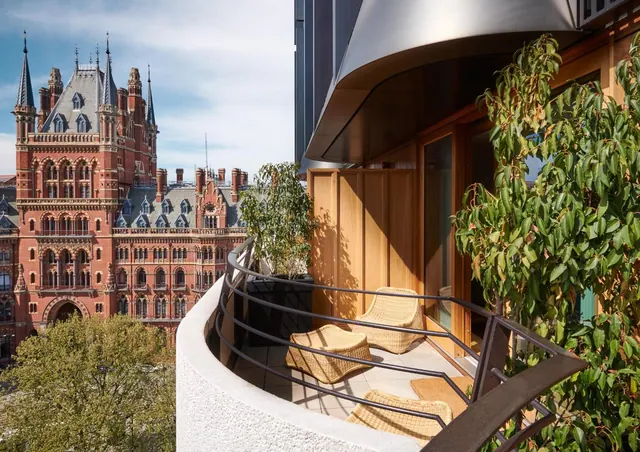 A balcony with wicker chairs and potted plants overlooks the red-brick Gothic facade of the St Pancras Renaissance Hotel.