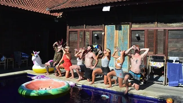 A group of people pose and drink on a wooden pool deck beside a small pool with inflatable floats.