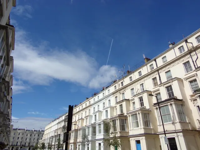 Upward view of cream-coloured terraced buildings with bay windows along a street under a clear blue sky.