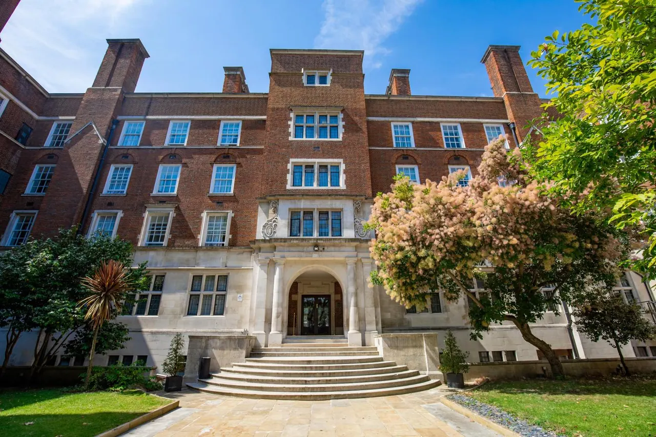 Front view of a red brick building with a stone portico, a flight of steps leading to the entrance, and trees and lawn in the foreground.