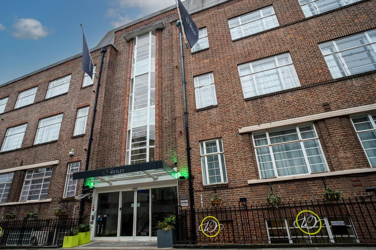 Low-angle view of a brick hotel building with a glass entrance canopy marked Wesley, flags on poles and black railings at street level.