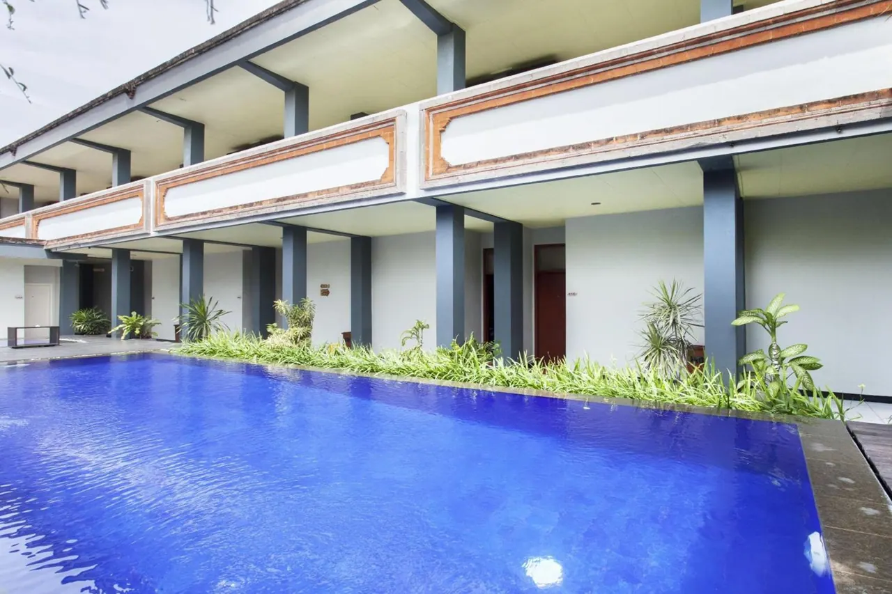 A blue rectangular swimming pool sits in front of a two-storey building with ground-floor rooms and a covered walkway.