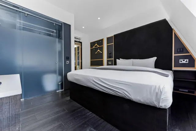 A bedroom with a large bed, black upholstered headboard, white bedding, a frosted glass sliding door and a wall-mounted air conditioning unit.