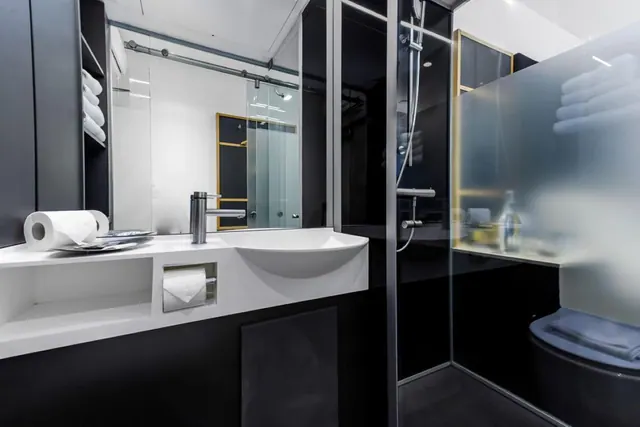 A black and white bathroom with a white basin, toilet roll, folded towels, and a glass-walled shower with a frosted panel.