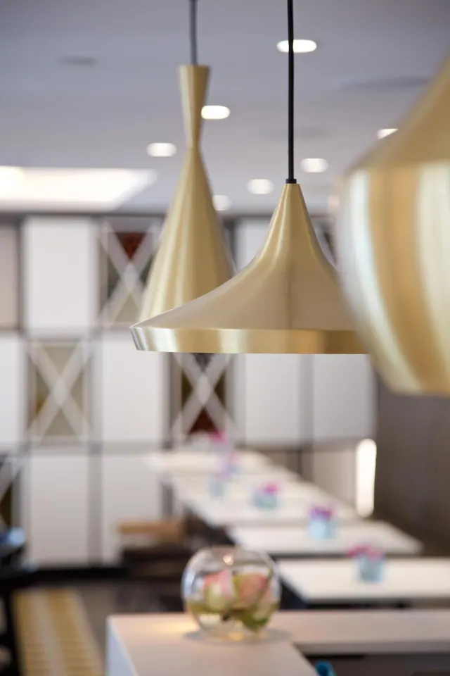 Brass pendant lamps hang above white tables with small flower arrangements in a restaurant dining area.