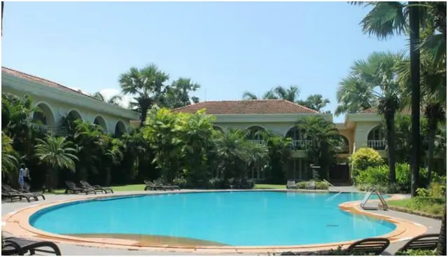 A large outdoor swimming pool is surrounded by sun loungers and tropical landscaping.
