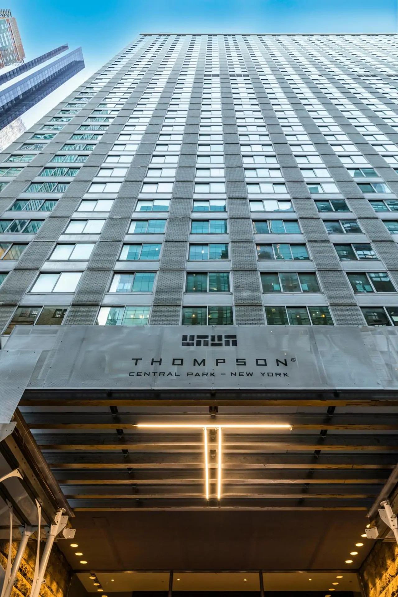 Low-angle view of the Thompson Central Park New York building facade, with its entrance canopy and illuminated signage at street level.