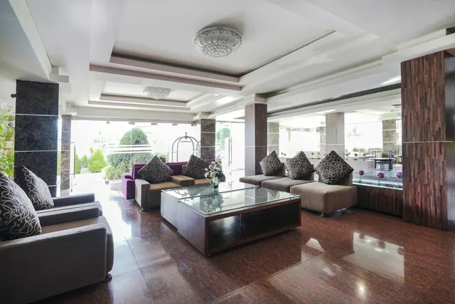 A lobby lounge with grey and patterned sofas around a glass-topped coffee table, with large windows looking out onto a garden.