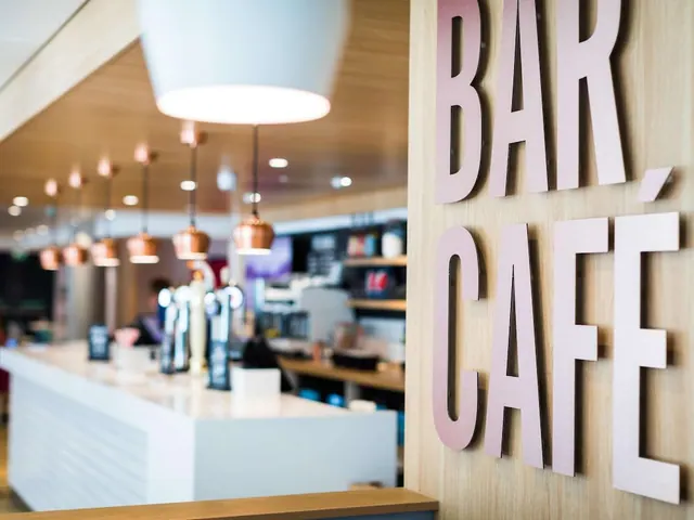 A bar and café counter with copper pendant lights, with the words BAR CAFE in large pink letters on a timber wall.