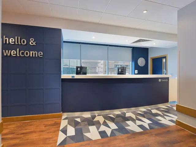 A curved blue reception desk stands in a lobby beside a blue wall with the lettering 'hello & welcome', above a geometric patterned floor.