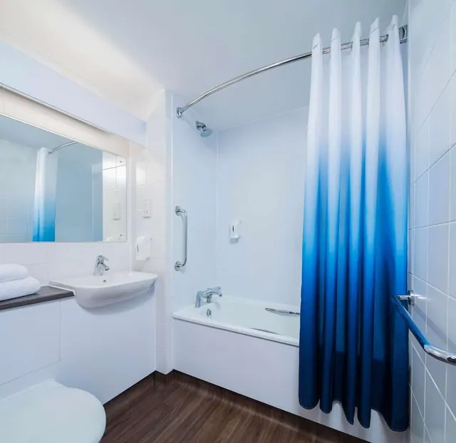 A bathroom with a wall-mounted sink, a bath with a blue gradient shower curtain, a grab rail on the wall, and a toilet at the lower left.