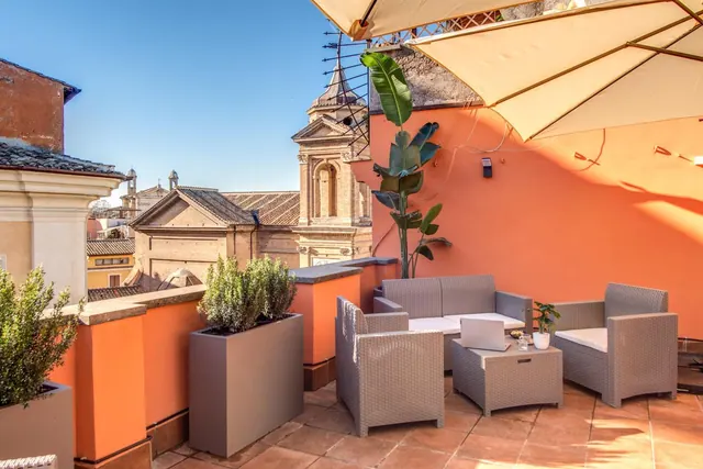 A furnished rooftop terrace with wicker seating, a parasol and a view over neighbouring rooftops and a church tower.