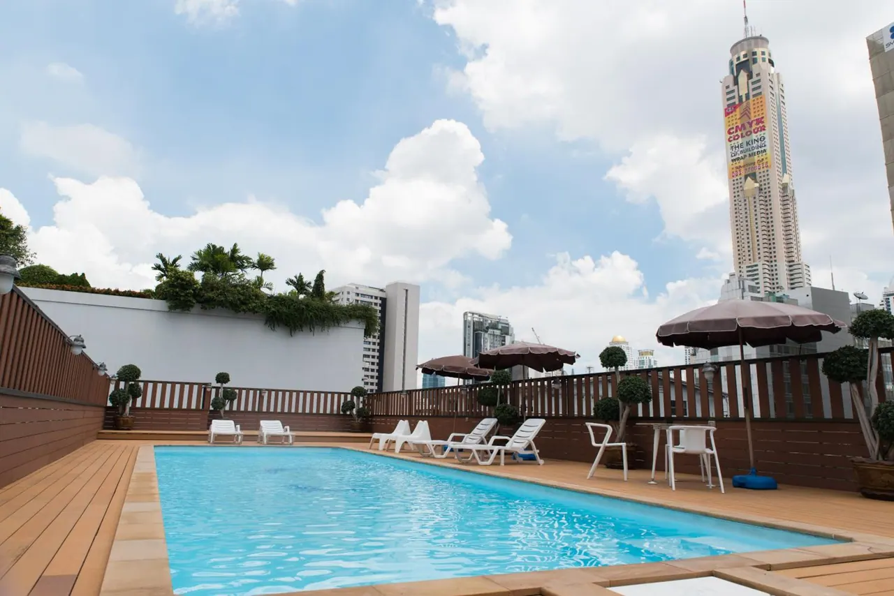 A rooftop swimming pool with white sun loungers, parasols and a tall city tower in the background.