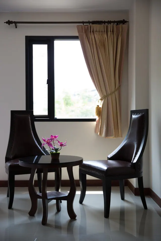 Two dark leather armchairs sit on either side of a small round side table with a pink orchid, beside a window with beige curtains.