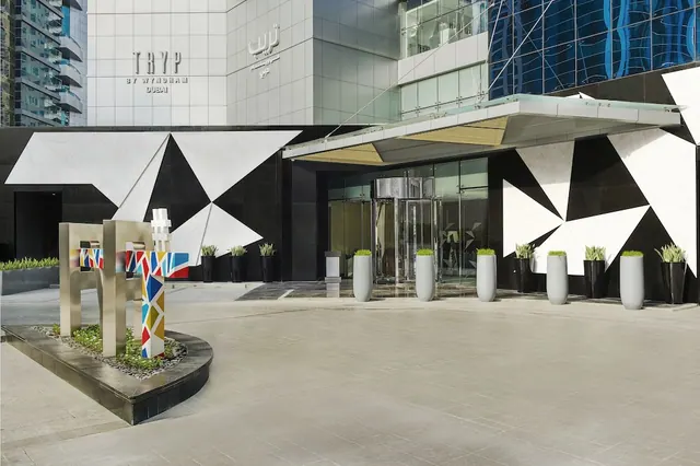 The front entrance of the TRYP by Wyndham Dubai hotel, with a glass canopy, revolving doors, planters and a colourful sculpture on the forecourt.
