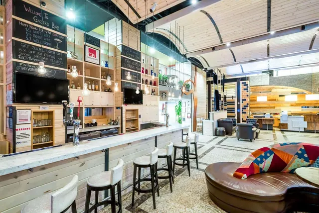 A bar counter with marble top, bar stools, chalkboard menus and a leather chaise lounge in a wood-panelled lounge area.