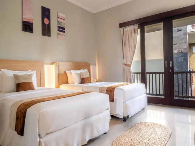 Two single beds with wooden headboards and white bedding sit in a room with framed wall art and glass doors opening onto a balcony.