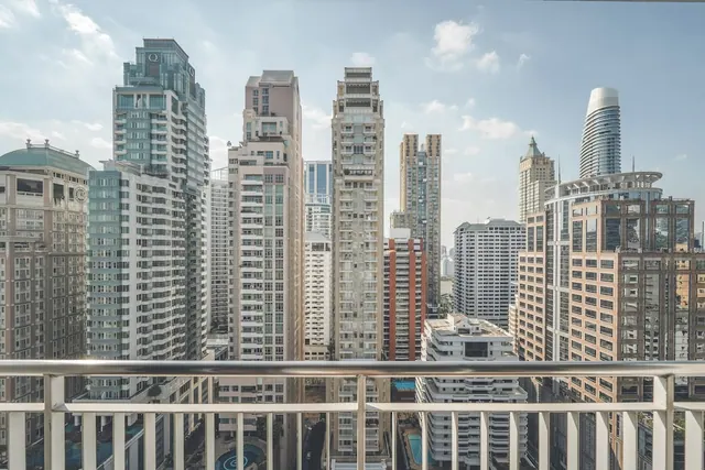 A view from a balcony railing over a dense cluster of high-rise residential and office towers under a hazy sky, with a pool visible below.