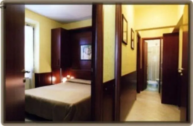 A bedroom with a double bed, a wooden wardrobe and lit bedside lamps, with a view down a hallway to a bathroom with a shower.