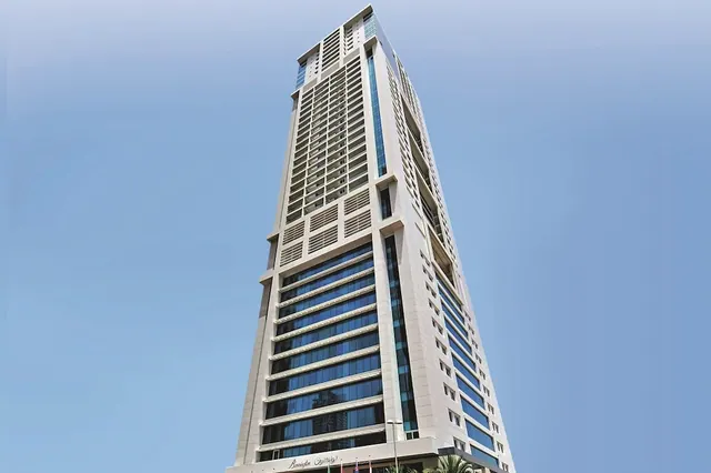 A low-angle view of a tall pale hotel tower with horizontal glass bands against a clear blue sky, with the hotel name sign visible at the base.