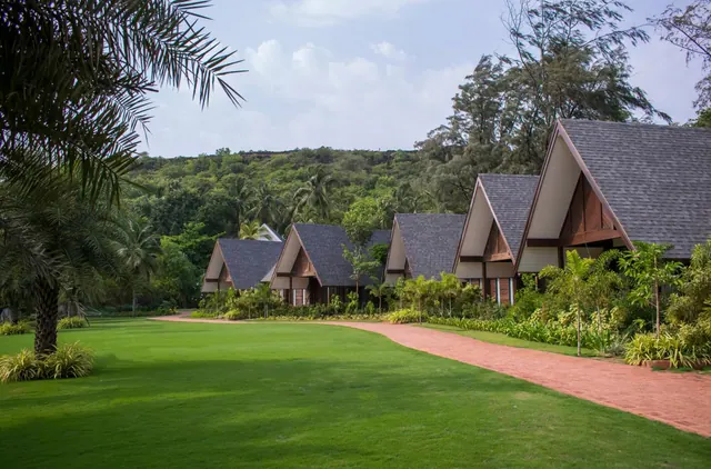A row of steep-roofed cottages borders a red-paved path across a manicured tropical garden.