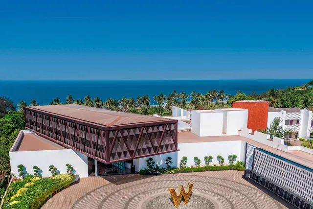 A modern hotel building and landscaped courtyard overlook the palm trees and sea.