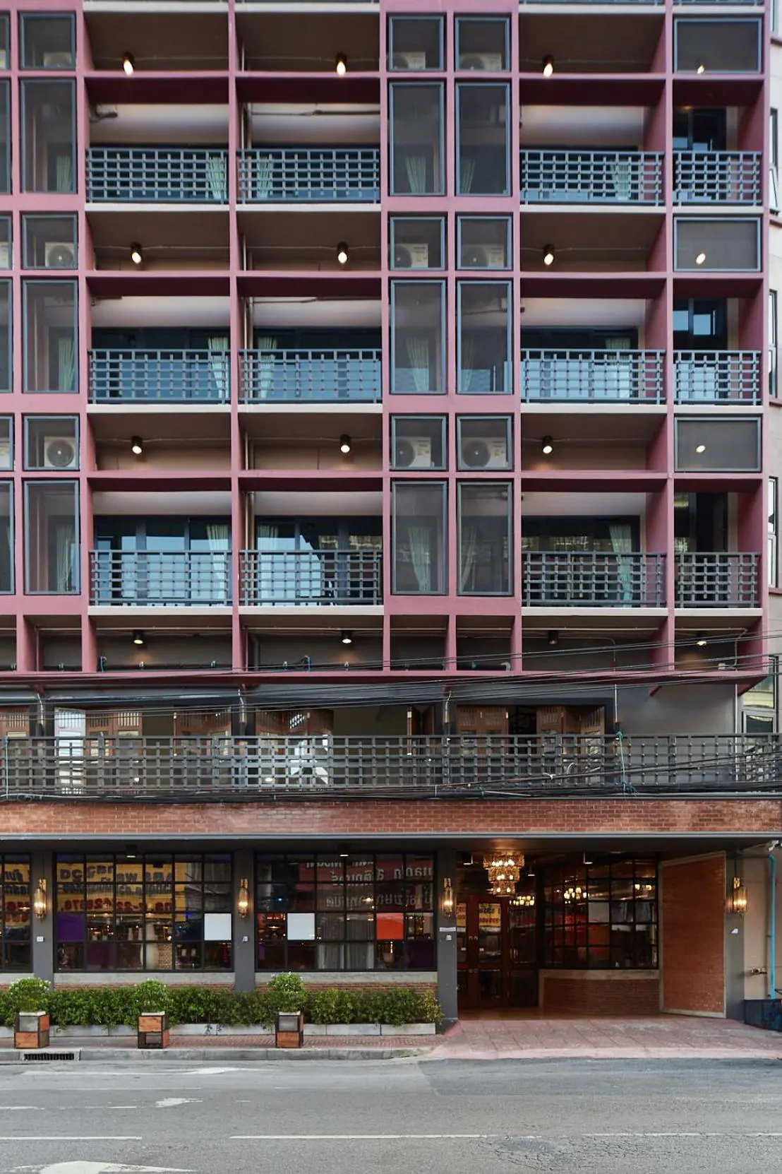 Front view of a pink multi-storey building with rows of balconies, a brick ground floor with a restaurant entrance, and a street with planters along the sidewalk.