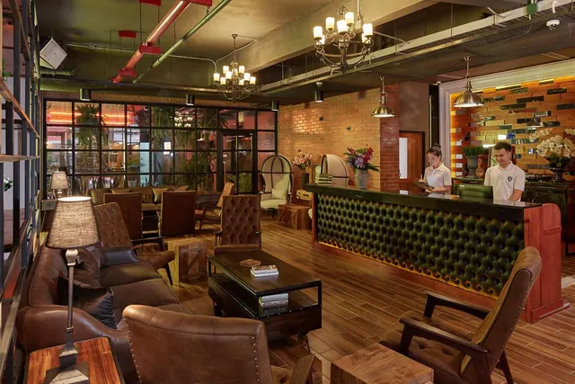 A lobby with brown leather sofas and armchairs, a tufted green reception desk, and two staff members behind the counter.