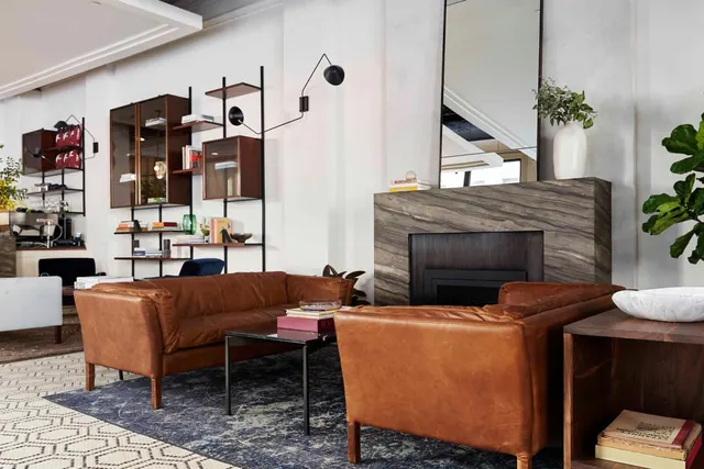A lounge seating area with two brown leather sofas, a low dark coffee table, a stone fireplace, a tall floor mirror and wall shelving.