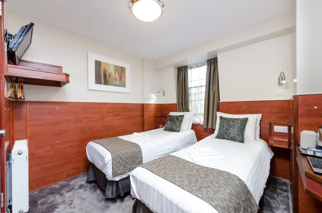 A twin bedroom with two single beds, wood-panelled lower walls, a wall-mounted television and a kettle on the right.