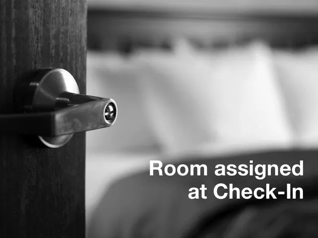 A black and white close-up of a metal lever door handle on a wooden door, with a blurred bed and white pillows behind it and the text overlay 'Room assigned at Check-In'.