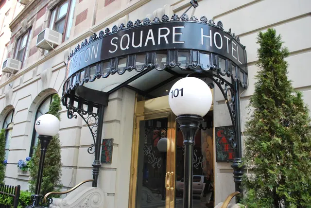 The entrance of the Washington Square Hotel, with a black curved awning sign, two white globe lamps and a tall evergreen beside the doors.