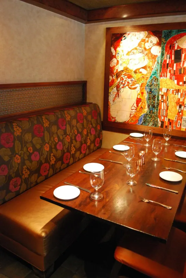 A set dining table with wine glasses and plates sits beside a leather and upholstered booth, with a large colourful mosaic-style artwork on the wall behind.