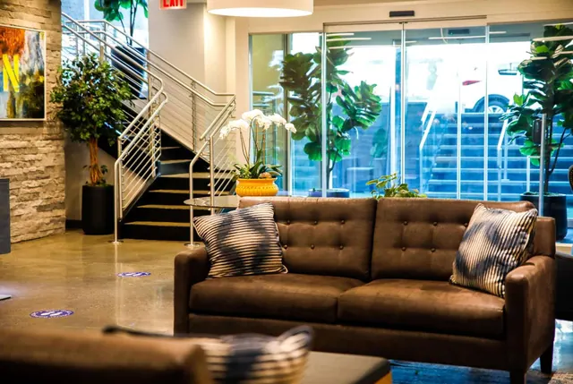 A hotel lobby with a brown tufted sofa and striped cushions, a staircase with metal railings, and glass doors looking out onto a street.