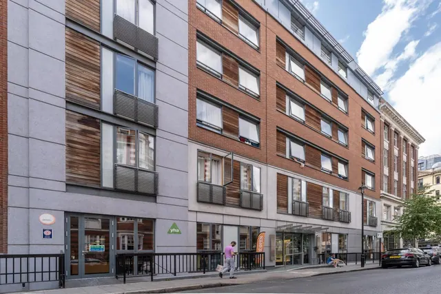 Street view of a multi-storey brick and render building with a YHA entrance at street level, with a pedestrian walking past and parked cars along the kerb.