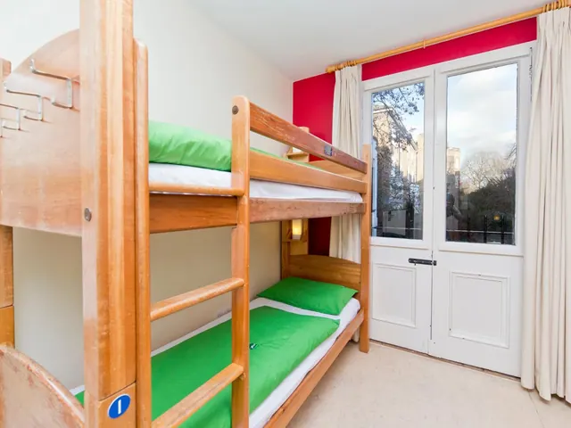 A bedroom with a wooden bunk bed with green bedding, a red accent wall, and glass French doors with cream curtains.