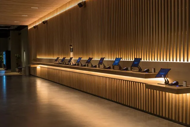A long wooden slatted reception counter with a row of tablet check-in stations, lit by warm lights in a lobby with no people visible.