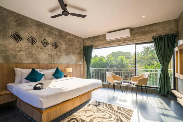 A bright bedroom with a double bed, seating beside a private balcony, and a garden view.